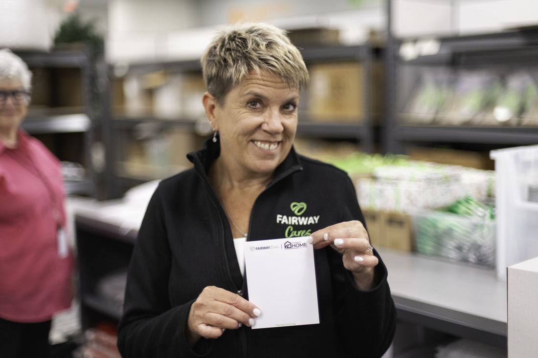 Sherri Anderson, CEO of Fairway Cares, smiling in the packing room and holding a blank Fairway Cares notecard