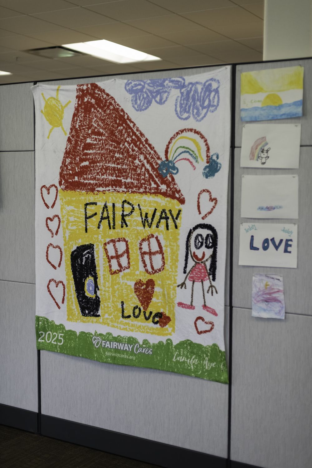 A Young at Art winning drawing — a house, hearts, and the word LOVE — printed on a Fairway Cares blanket and hung proudly in the office